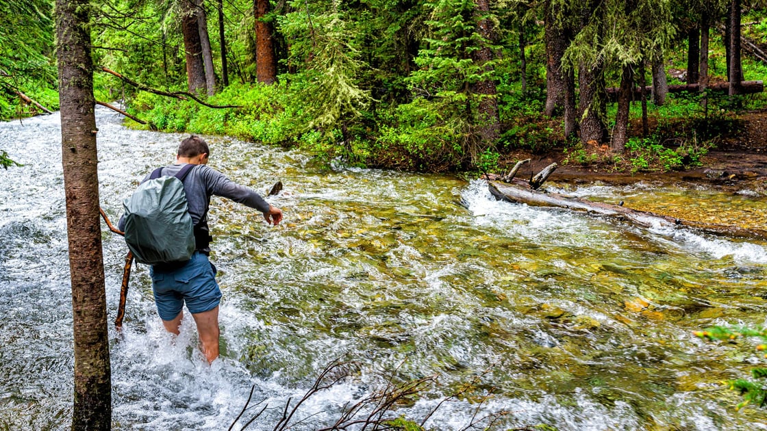 hiker-crossing-swollen-creek