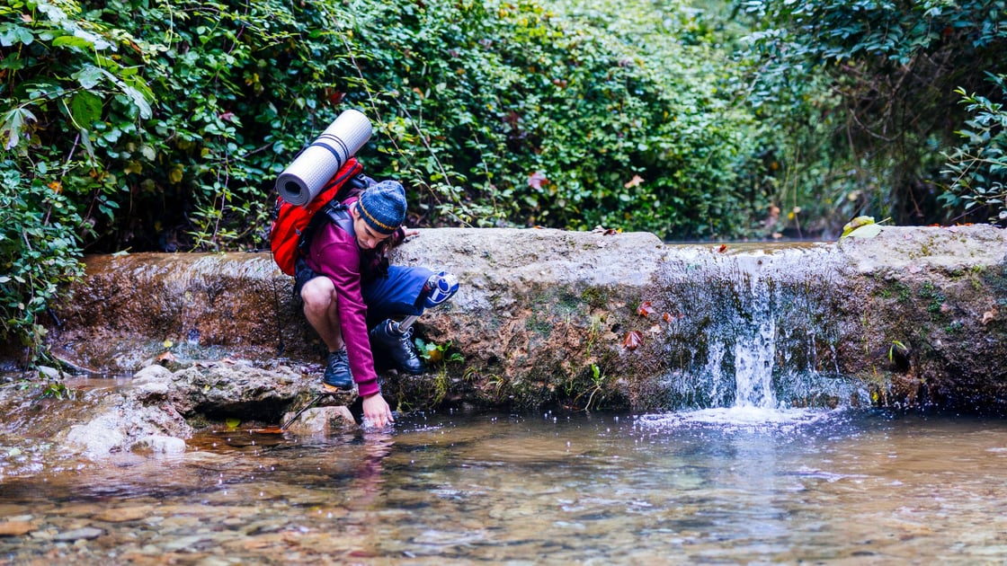 young-man-dipping-cup-in-river